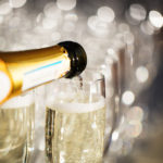 close up of a bottle pouring champagne into glasses with blurred background